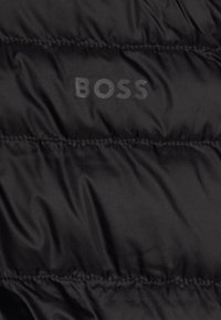 Giacca imbottita nera con una texture liscia e lucida, sezioni trapuntate e un sottile logo "BOSS" in stampa tonale.