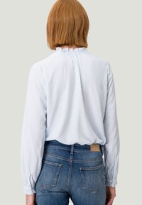 Helles blau gestreiftes Blusenshirt mit einem Rüschenausschnitt und geknöpften Manschetten, kombiniert mit blauen Jeans aus Denim mit Gesäßtaschen.