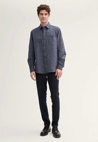 Chemise à manches longues bleu marine avec tissu texturé, une poche poitrine unique et un col, associée à un pantalon noir et des chaussures noires.