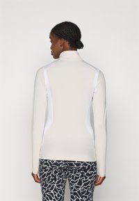 Lichtbeige lange mouw top met een hoge kraag, voorzien van witte zijpanelen en een aansluitend ontwerp. Gepaard met gestreepte zwarte broek.