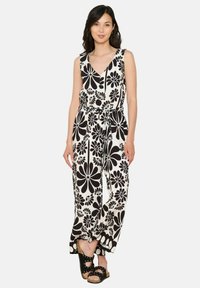 Črno-bela cvetlična kombinezona z V-izrezom, brez rokavov, z zategnjenim pasom, širokimi hlačnicami in zavezanim pasom. Ponaša se z drznimi cvetličnimi vzorci.