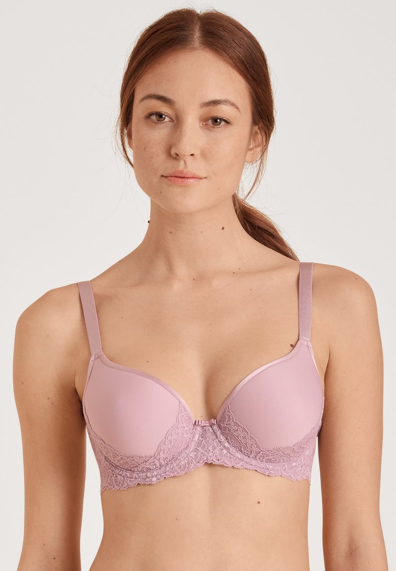 Lichtroze bh met gladde cups en delicate kantdetails op de band, verstelbare bandjes en een haaksluiting aan de voorkant.