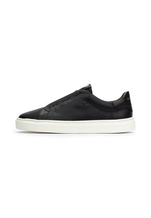 Zapatilla slip-on de cuero negra con un acabado texturizado, suela de goma blanca y detalles de costura mínimos. Presenta una puntera redondeada y un diseño de perfil bajo.