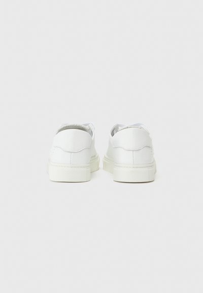 Valkoiset nahkakengät, joissa on sileä pinta, pyöristetty muoto ja paksu kumipohja. Ominaisuuksia ovat minimaalinen ompelu ja matala leikkaus.