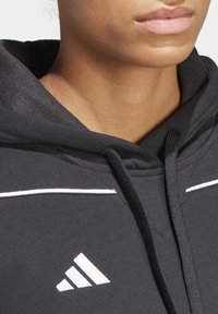 Zwarte hoodie met een gladde textuur, voorzien van een witte accentlijn en een geborduurd Adidas-logo. Kap en koordjes zijn zichtbaar.