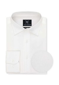 Biała slim-fit koszula z klasycznym kołnierzykiem, z przodu z guzikami i pojedynczym zaokrąglonym mankietem. Towarzyszy jej okrągły próbnik materiału.