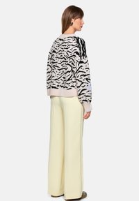 Gestrickter Pullover mit einem Zebra-Muster in Schwarz und Beige, langen Ärmeln und gerippten Bündchen. Kombiniert mit hochtaillierten, blassgelben Hosen mit weitem Bein.
