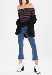 Top de rayas sin hombros en negro, rojo y blanco, combinado con unos vaqueros acampanados azules con puños deshilachados y sandalias de tacón blancas con cremalleras.