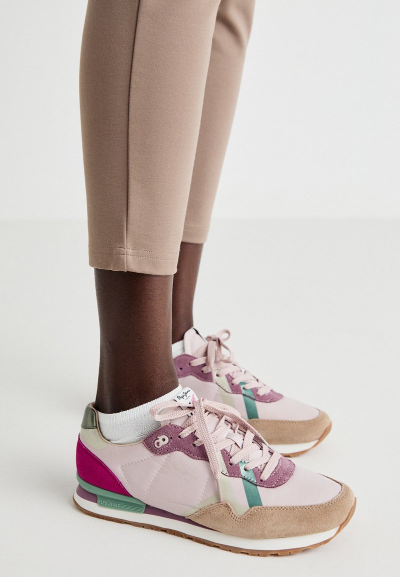 Sneakers mit einem rosa und beigen Design, bestehend aus Wildleder und Stoffmaterialien, Pastellakzenten und einer strukturierten Sohle. Schnürstil mit Branding.