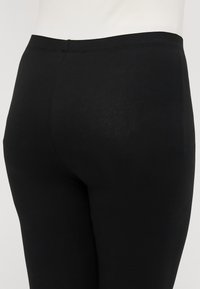 Zwarte leggings gemaakt van gladde, rekbare stof. Ze hebben een hoge tailleband en een aansluitende pasvorm, met minimale naden en geen zichtbare patronen.