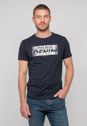 T-shirt en coton bleu marine avec un logo graphique et un texte rouge et argenté qui indique "TRUE BLUE DENIM". Manches courtes et col rond.