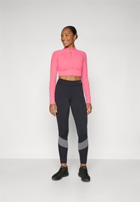 Pink long-sleeve cropped zip jacket paired with high-waisted black leggings featuring gray accents. Model wears black athletic shoes.