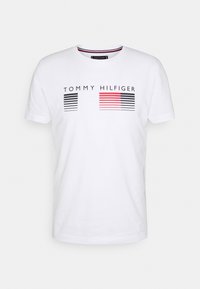 Camiseta de manga corta blanca con el logo "TOMMY HILFIGER" en negro y rojo, con acentos de rayas horizontales. Material de algodón, diseño de cuello redondo.