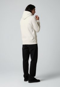 Cream-colored hoodie with a relaxed fit, adjustable drawstring hood, ribbed cuffs, and black jeans. Smooth texture and minimalistic design.