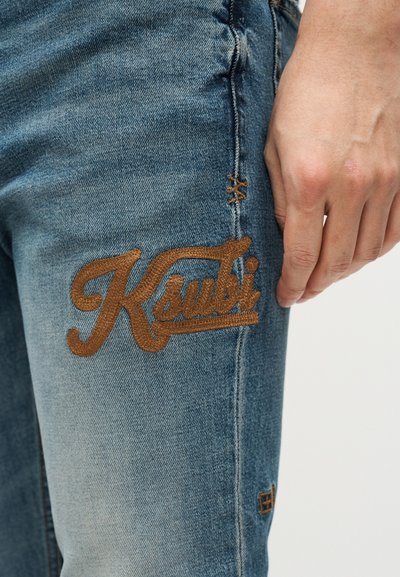 Μπλε τζιν παντελόνι από denim με καφέ κεντημένο λογότυπο "Ksubi" στο αριστερό μηρό, με φθαρμένες λεπτομέρειες κοντά στις ραφές.