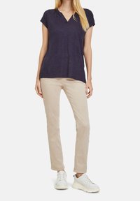 Námořnické tričko s výstřihem do V a krátkým rukávem, spárované se světlými slim-fit kalhotami a bílými teniskami. Materiál vypadá měkce a má uvolněný střih.
