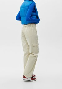 Pantalones cargo beige con cintura elástica, bolsillos laterales y un corte relajado, combinados con un chaleco acolchado azul y zapatillas rojas y blancas.