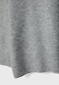 Tissu en maille grise douce avec ourlet côtelé, montrant la texture et de légers plis au bas d’un vêtement.