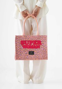 Sac fourre-tout à imprimé léopard en rose et orange avec "SUPER WOMAN" en rouge vif. Doté de deux poignées supérieures et d'une étiquette de marque noire en bas.