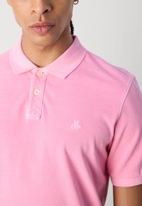 Rosa bomulls polo skjorte med korte ermer, tre-knapps placket, og en liten hvit logo på venstre bryst. Slitesterk tekstur, klassisk design.