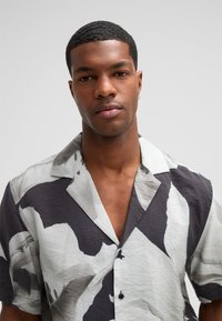 Koszula z krótkim rękawem z lekkiego materiału, prezentująca odważny czarno-biały abstrakcyjny wzór, z kołnierzykiem z wcięciem i detalem w postaci guzika.