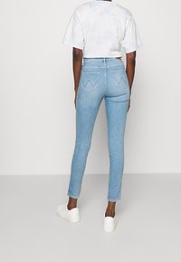 Ljusblå skinny jeans med hög midja, med en 5-fickorsdesign och distinkt sömnad på bakfickorna. Bar med en kortärmad tie-dye topp och vita sneakers.