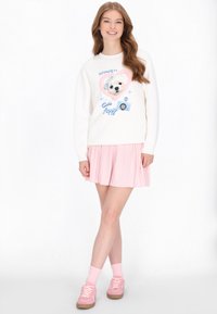 Weißer Pullover mit einer Cartoon-Hund-Grafik in einem rosa Herz, kombiniert mit einem hellrosa plissierten Rock und rosa Sneakern. Weicher Stoff, lässiges Design.