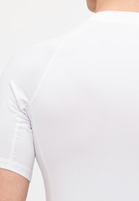 Hvit tettsittende treningstrøye med korte ermer, laget av glatt, elastisk materiale. Har flate sømmer og et enkelt, strømlinjeformet design.