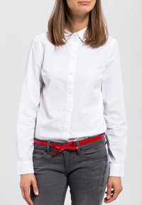 Hvit skjorte med klassisk krage, kombinert med mørk grå jeans og et lyst rødt belte. Glatt stofftekstur, tettsittende design.