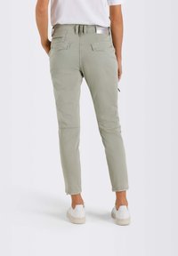 Ljust gröna, avsmalnande byxor med fickor, en flexibel midja och dragkedjor vid anklarna, ihop med vita sneakers på en modell.