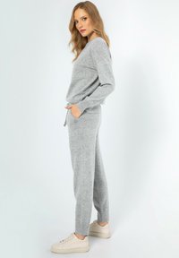 Grijze trui en bijpassende sweatpants gemaakt van zacht breiwerk. De sweatpants hebben zakken en een aansnoerbare tailleband. Gepaard met beige sneakers.