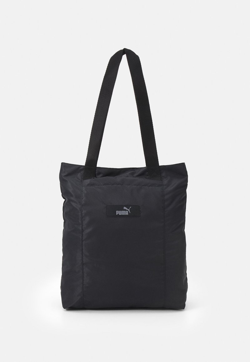 Bolsa tote de nailon negra con dos asas resistentes, de forma rectangular y con un pequeño parche de logo en la parte frontal. Textura suave.