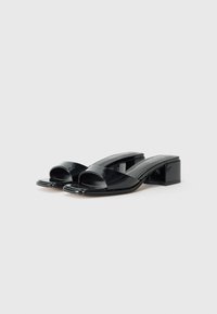 Black patent leather open-toe mules with a square toe, wide cross strap, and a low block heel. Smooth, glossy texture with minimalist design.
