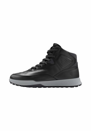 Zapatilla negra impermeable de caña alta con suela gruesa gris y cierre de cordones en la parte delantera, mostrando perfil lateral sobre fondo blanco.