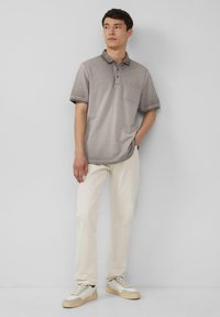 Grijze poloshirt met een zak, zwart kraagtrim en korte mouwen, gecombineerd met crèmekleurige broek en beige sneakers.
