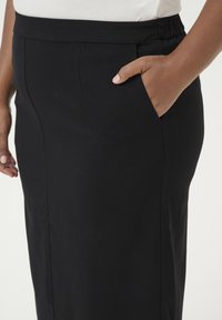Falda negra, de longitud a la rodilla, hecha de una tela suave. Presenta una cinturilla elástica y bolsillos laterales. Diseño simple de corte recto.