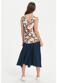 Haut fleuri de couleur crème avec des touches orange et bleu marine, doté d'une ouverture en forme de trou de serrure dans le dos. Associé à une jupe fluide bleu foncé et des baskets blanches.