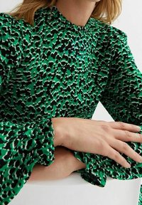 Vihreä pusero, jossa mustavalkoinen eläinkuvio, liehukehihat ja korkea kaulus. Kangas on sileä ja kevyt.