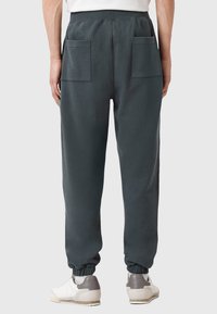 Donkergrijze sweatpants met een elastieke tailleband, twee achterzakken en taps toelopende boorden, gecombineerd met wit en grijs sneakers.