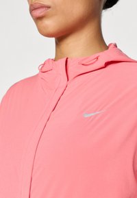 Ελαφρύ ροζ hoodie με φερμουάρ στο μπροστινό μέρος, ρυθμιζόμενο σκέπαστρο με κορδόνι και αντανακλαστικό ασημί λογότυπο Nike στο στήθος. Ομαλή υφή.