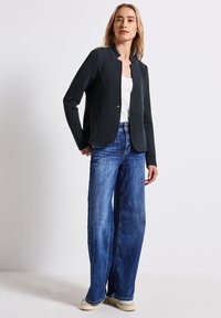 Kollsvart figursydd kavaj med rund halsringning, enkel knappstängning, strukturväv; ihop med ljusblå vida jeans och beige skor.