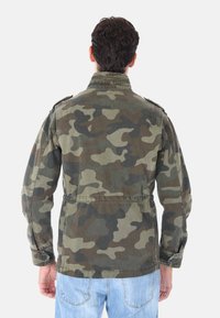 Giacca camouflage in verde oliva, marrone e nero. Caratterizzata da un collo strutturato, spalline e polsini con bottoni. Tessuto in cotone.