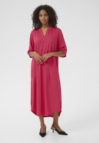 Long, loose-fitting dress in bright pink fabric, featuring a V-neckline, three-quarter sleeves, and side pockets. Mid-calf length, smooth texture.