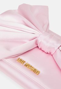 Růžová saténová kabelka přes rameno s velkou mašlí a zlatým logem "LOVE MOSCHINO". Hladký povrch s pevným tvarem a elegantním designem.