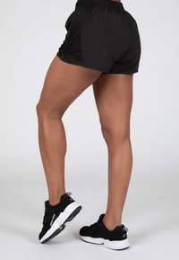 Zwarte atletische shorts met een ademend mesh ontwerp, voorzien van een elastische tailleband en zijsplitten, gecombineerd met zwart-witte hardloopschoenen.