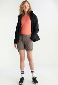 Sort vandtæt jakke over en orange t-shirt, med khaki shorts og sorte sneakers. Hvide sokker med sorte striber. Afslappet udendørs outfit.