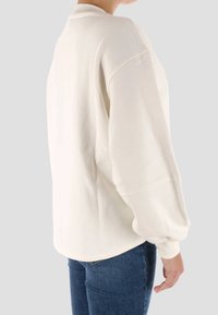 Felpa color crema con vestibilità rilassata, maniche lunghe con polsino e orlo curvo, realizzata in un tessuto morbido e liscio.