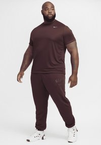 Bruna Nike träningskläder, med t-shirt med kort ärm och joggers. Slät tyg med diskreta logotyper. Vita träningsskor med svarta detaljer.