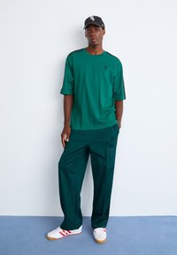 Grøn kortærmet t-shirt med sorte sidedele, parret med matchende grønne bukser. Hvide sneakers med røde striber fuldender outfittet.