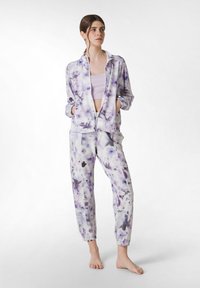 Lila tie-dye träningsdräkt gjord av mjukt material, med en zip-up jacka med två fickor och elastiska ärmslut, i kombination med avsmalnande byxor.